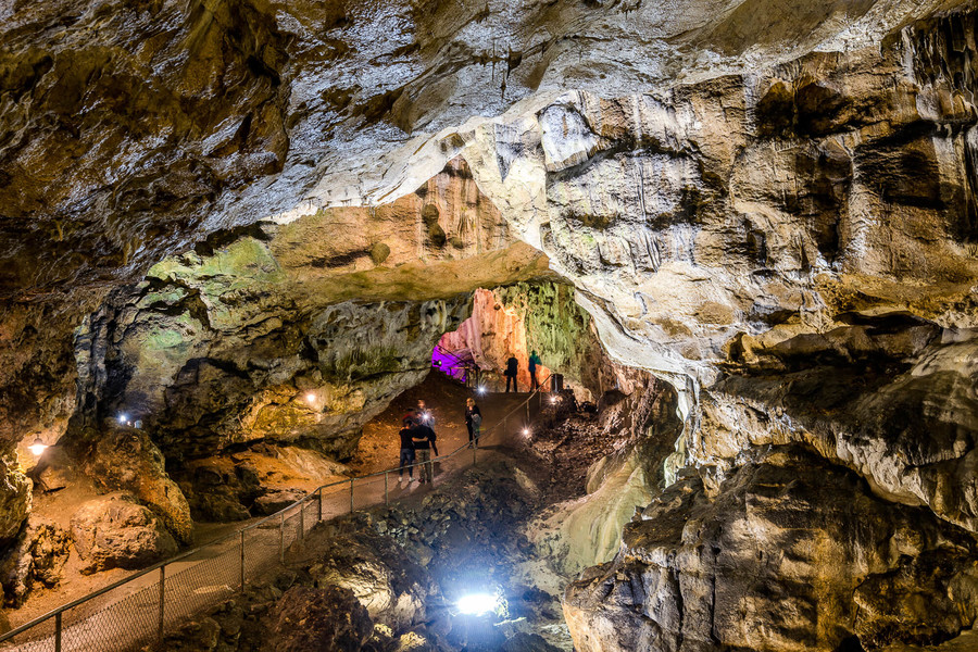 Eine große Höhle von innen. In der Mitte laufen auf einem befestigten Weg einige Besuchende.
