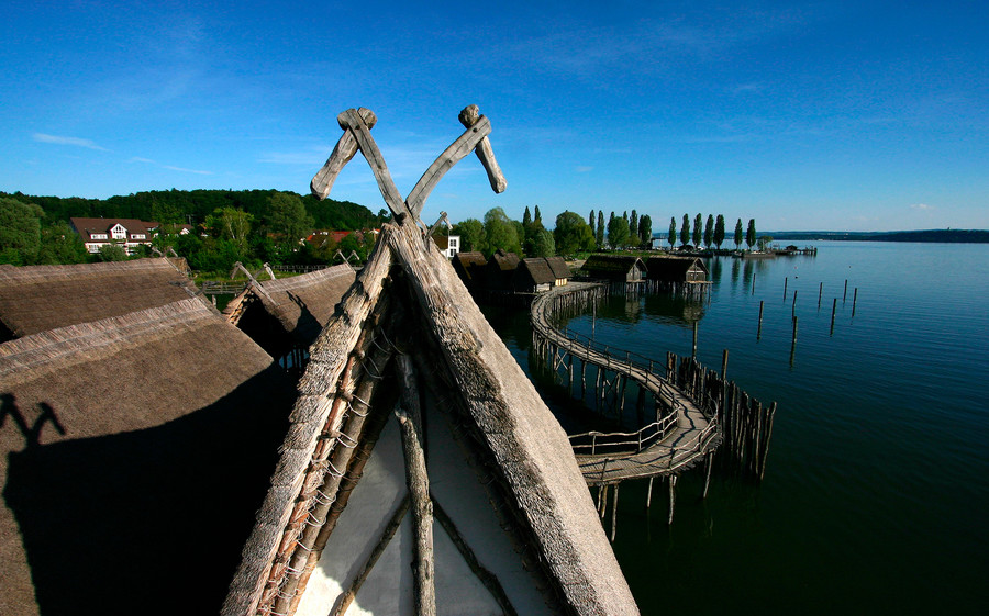 Am Ufer des Bodensees liegen die Pfahlbauten. Durch einen Holzsteg sind die Bauten miteinander verbunden.